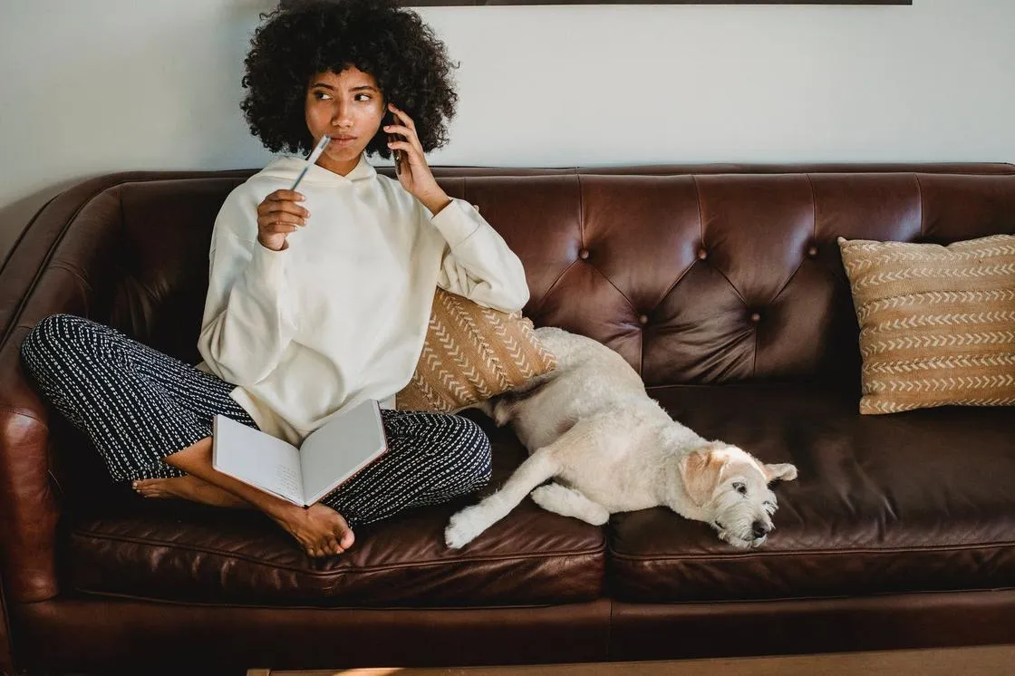 Девушка на кожаном диване рядом с собакой с дневником на руках