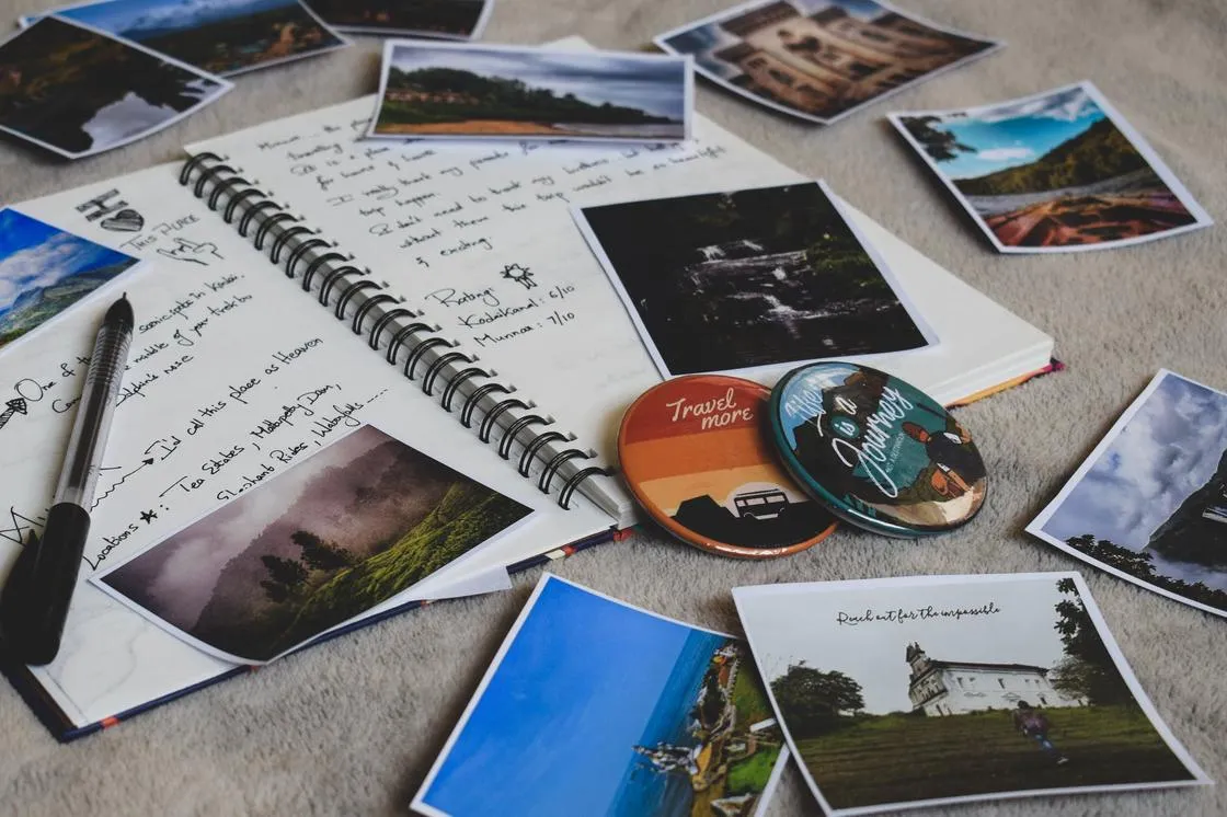 Дневник с записями, ручка, сувенирные магниты и фотографии из путешествий на поверхности стола